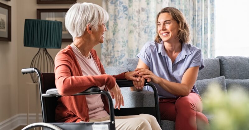 A caregiver holding an olde client's hand in their wheelchair represents personal care in Johnston County.