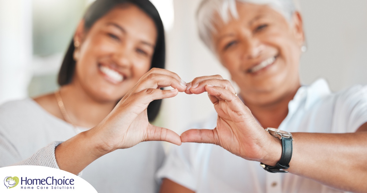 A daughter and an older mother create a heart with their hands, representing the feeling that is highlighted during National Family Caregivers Month