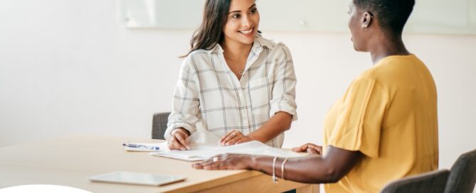 A woman happily interviews another woman, representing how well caregiver interviews can go when prepared.