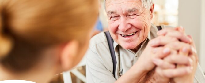 A caregiver holds hands with a happy older client, representing the results of creating a comfortable environment in the home.