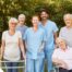 2 caregivers and seniors smile while in a group representing how caregivers can facilitate socialization.